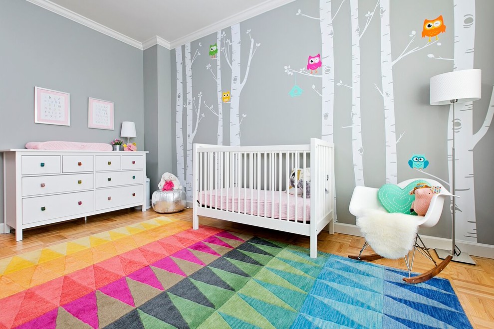 Photo of a mid-sized contemporary nursery for girls in New York with grey walls, multi-coloured floor and light hardwood floors.