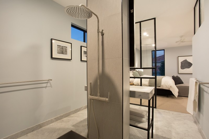 Photo of a mid-sized industrial master wet room bathroom in Gold Coast - Tweed with furniture-like cabinets, black cabinets, a japanese tub, a wall-mount toilet, gray tile, porcelain tile, white walls, marble floors, a trough sink, marble benchtops, white floor and an open shower.