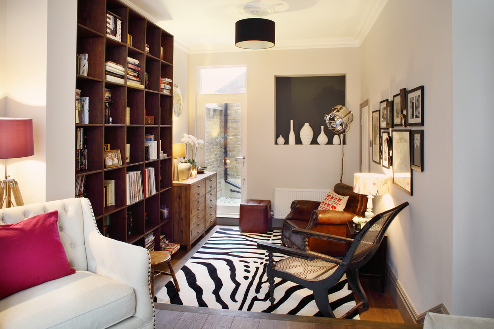 Inspiration for a small eclectic enclosed living room in London with a library, white walls, medium hardwood floors and brown floor.