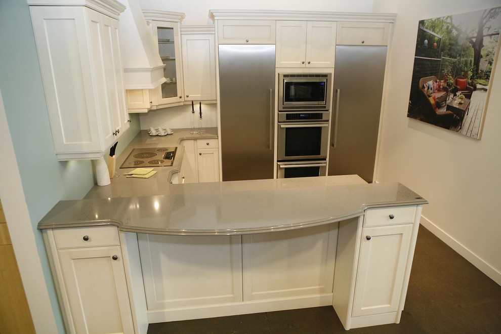 Example of a mid-sized transitional u-shaped concrete floor and brown floor kitchen design with shaker cabinets, white cabinets, stainless steel appliances and a peninsula