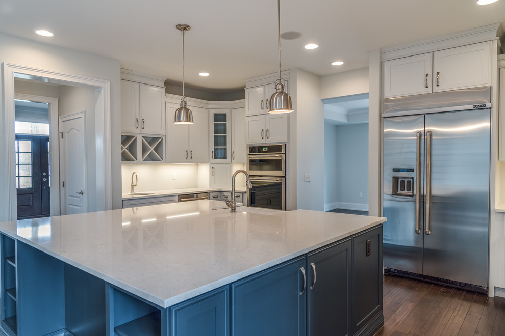 Example of a large transitional u-shaped dark wood floor and brown floor kitchen design with a farmhouse sink, shaker cabinets, blue cabinets, quartzite countertops, stainless steel appliances and an island
