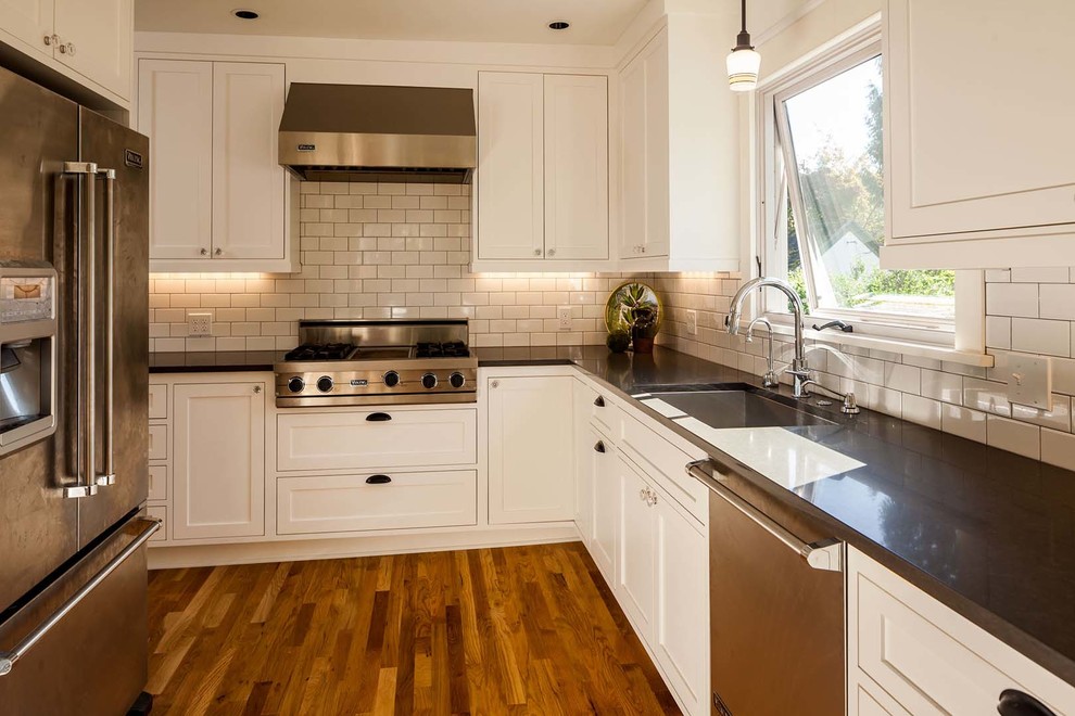 Large transitional dark wood floor kitchen photo with a drop-in sink, recessed-panel cabinets, white cabinets, granite countertops, white backsplash, subway tile backsplash, stainless steel appliances and an island