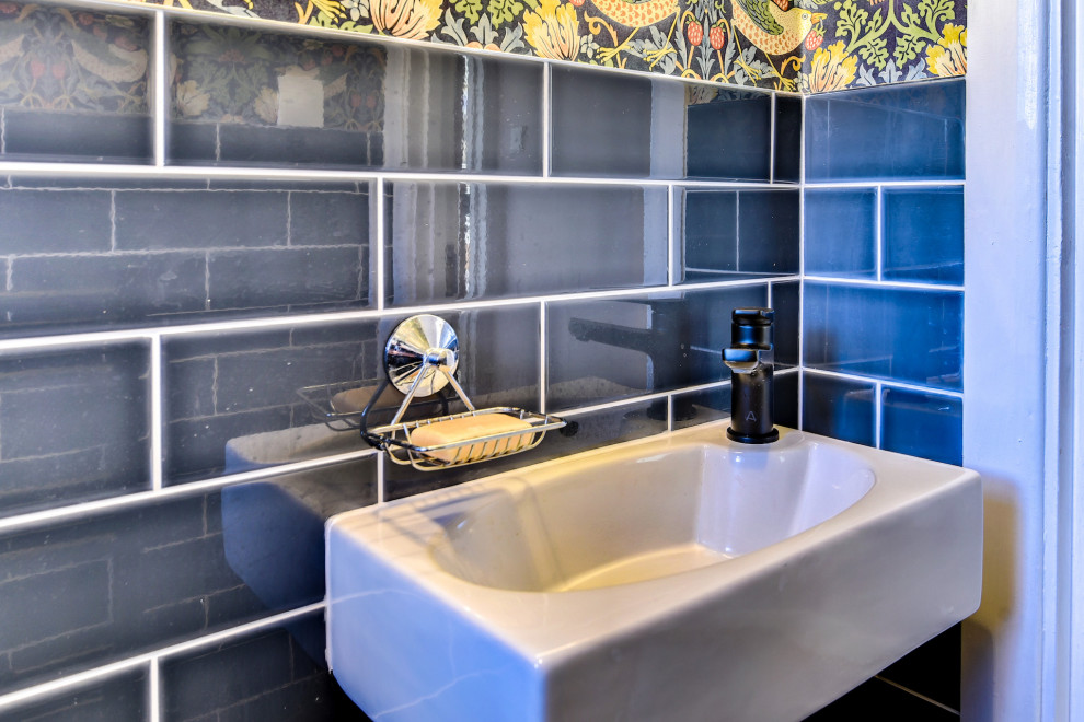 Inspiration for a small eclectic cloakroom in Sussex with a wall mounted toilet, blue tiles, ceramic tiles, multi-coloured walls, porcelain flooring, a wall-mounted sink, grey floors, feature lighting and wallpapered walls.