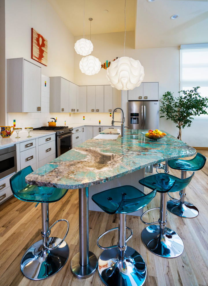 Inspiration for a mid-sized contemporary l-shaped eat-in kitchen in Denver with a farmhouse sink, flat-panel cabinets, white cabinets, quartzite benchtops, white splashback, mosaic tile splashback, stainless steel appliances, medium hardwood floors, with island, multi-coloured floor, turquoise benchtop and vaulted.