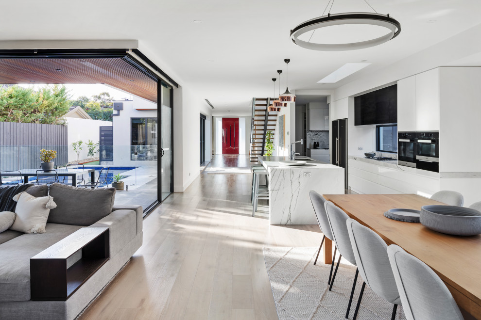 Photo of a large modern open plan dining in Melbourne with white walls, light hardwood floors, a standard fireplace, a plaster fireplace surround and beige floor.