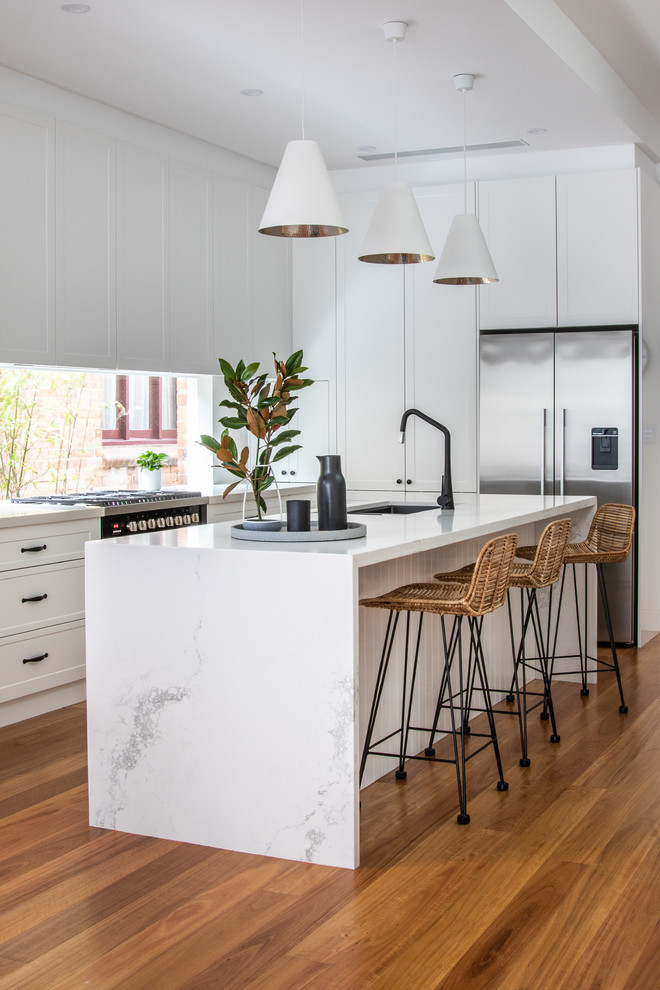 Inspiration for a contemporary l-shaped eat-in kitchen in Sydney with white cabinets, quartz benchtops, window splashback, an undermount sink, recessed-panel cabinets, stainless steel appliances, medium hardwood floors, with island, brown floor and white benchtop.