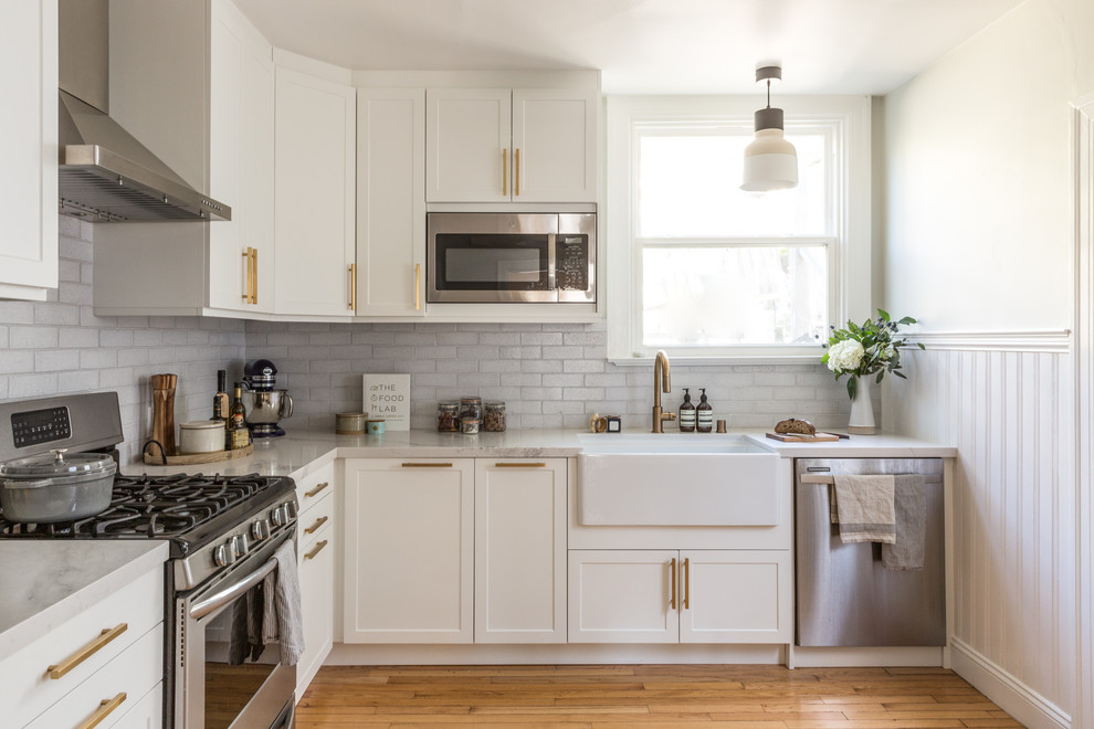 Design ideas for a small transitional l-shaped separate kitchen in San Francisco with white cabinets, white splashback, brick splashback, stainless steel appliances, light hardwood floors, no island, beige floor and beige benchtop.