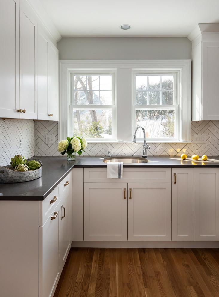 Mid-sized transitional u-shaped light wood floor and brown floor enclosed kitchen photo in Boston with an undermount sink, shaker cabinets, white cabinets, quartz countertops, gray backsplash, ceramic backsplash, stainless steel appliances, a peninsula and gray countertops