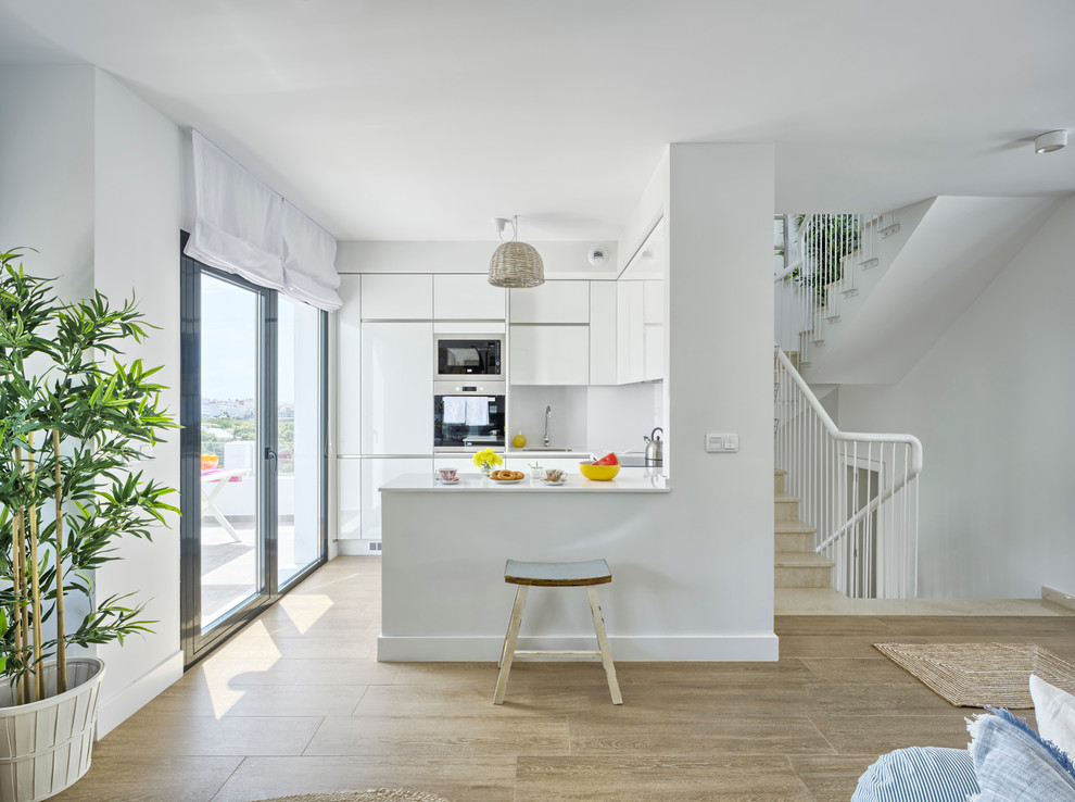Small beach style u-shaped open plan kitchen in Malaga with a drop-in sink, flat-panel cabinets, white cabinets, quartz benchtops, white splashback and porcelain floors.
