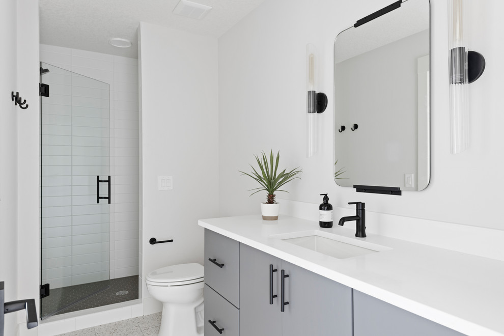 Design ideas for a transitional 3/4 bathroom in Minneapolis with flat-panel cabinets, grey cabinets, an alcove shower, white tile, white walls, an undermount sink, grey floor, a hinged shower door and white benchtops.