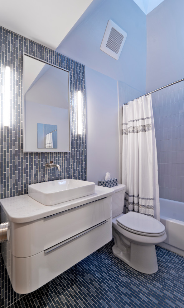 This is an example of a medium sized retro ensuite bathroom in DC Metro with flat-panel cabinets, medium wood cabinets, an alcove bath, a shower/bath combination, a two-piece toilet, green tiles, ceramic tiles, white walls, mosaic tile flooring, a vessel sink, engineered stone worktops, blue floors, a shower curtain, white worktops, a wall niche, a single sink, a floating vanity unit, a vaulted ceiling and wainscoting.