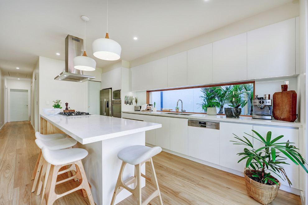 Design ideas for a large scandinavian galley open plan kitchen in Sydney with an undermount sink, flat-panel cabinets, white cabinets, quartz benchtops, white splashback, glass sheet splashback, stainless steel appliances, light hardwood floors, with island, brown floor and white benchtop.