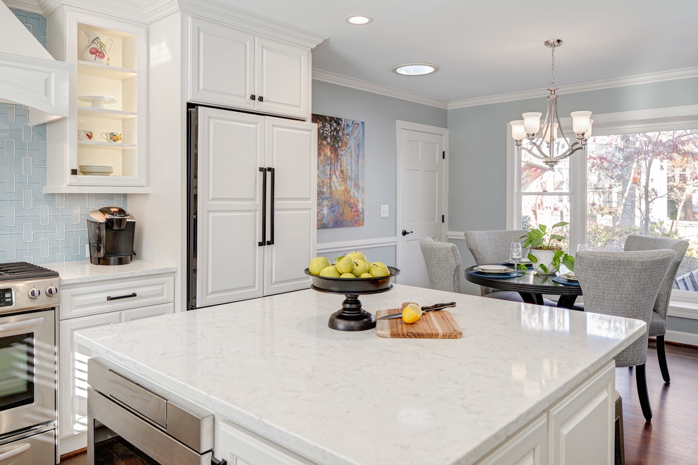 Example of a mid-sized transitional u-shaped medium tone wood floor and brown floor eat-in kitchen design with a farmhouse sink, raised-panel cabinets, white cabinets, quartz countertops, blue backsplash, porcelain backsplash, paneled appliances and an island