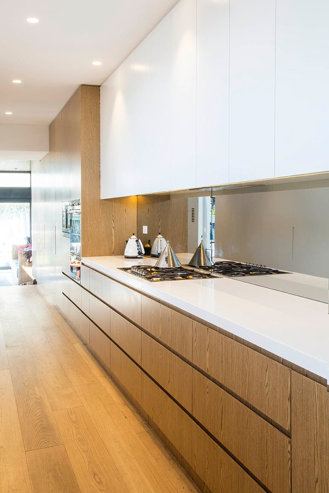 Large contemporary galley kitchen pantry in Sydney with a drop-in sink, solid surface benchtops, mirror splashback, stainless steel appliances, medium hardwood floors and no island.