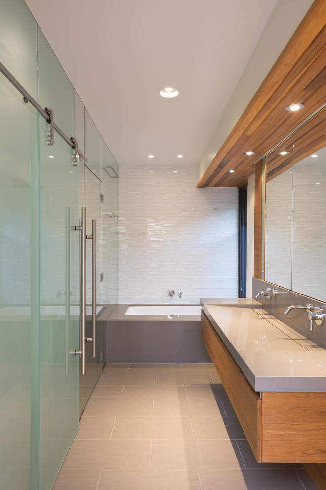 Mid-sized contemporary master bathroom in Toronto with an integrated sink, furniture-like cabinets, medium wood cabinets, engineered quartz benchtops, an undermount tub, a curbless shower, a one-piece toilet, gray tile, glass tile, white walls and porcelain floors.