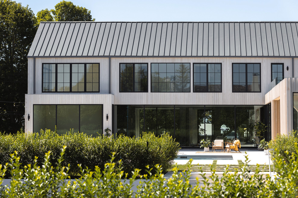 Стильный дизайн: большой, бежевый частный загородный дом в стиле модернизм с двускатной крышей, металлической крышей и черной крышей - последний тренд