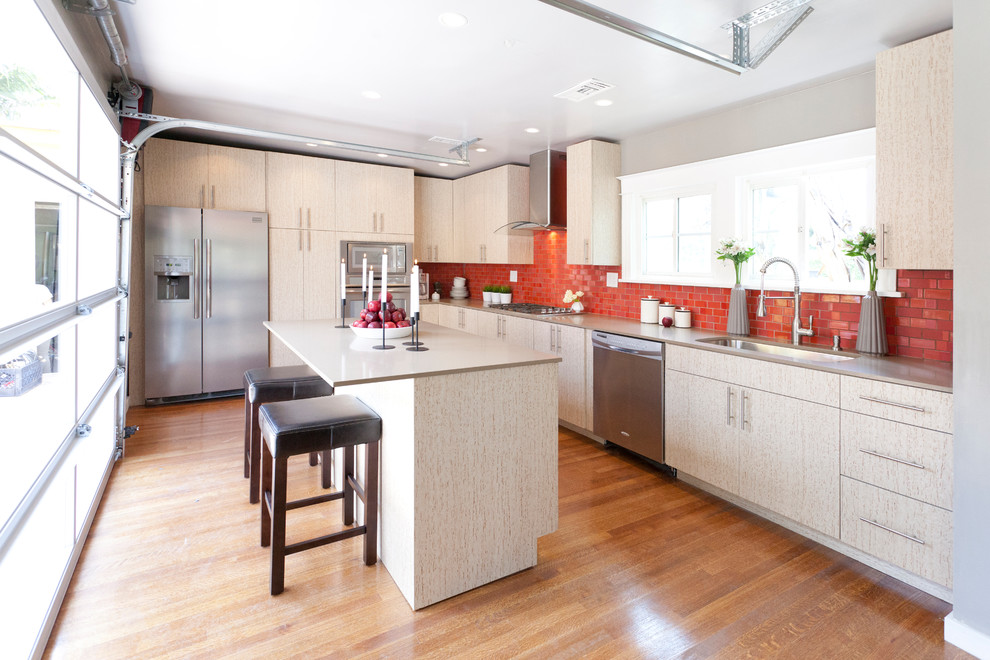This is an example of a contemporary l-shaped kitchen in New York with flat-panel cabinets, light wood cabinets, red splashback, subway tile splashback and stainless steel appliances.