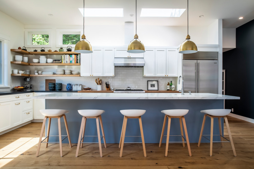 Photo of a small traditional l-shaped open plan kitchen in San Francisco with shaker cabinets, white cabinets, marble worktops, white splashback, metro tiled splashback, white appliances, an island, white worktops, a submerged sink, light hardwood flooring and beige floors.