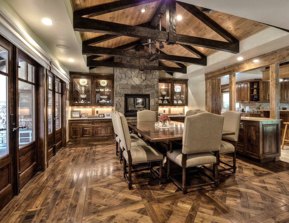 Example of a large mountain style medium tone wood floor kitchen/dining room combo design with white walls, a standard fireplace and a stone fireplace