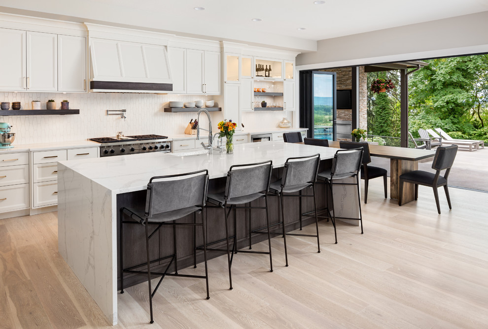Eat-in kitchen - transitional l-shaped light wood floor and beige floor eat-in kitchen idea in DC Metro with a farmhouse sink, recessed-panel cabinets, white cabinets, white backsplash, an island and white countertops