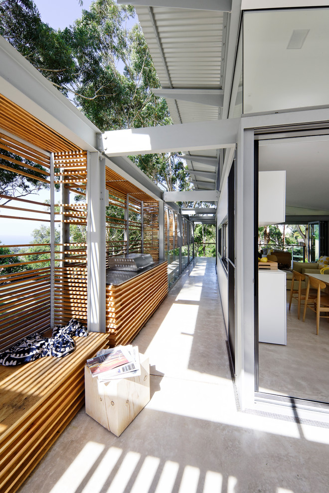 This is an example of a large contemporary side yard screened-in verandah in Sydney with a roof extension, glass railing and concrete slab.