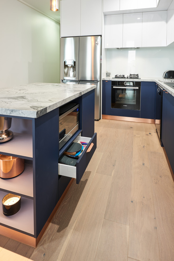 This is an example of a small contemporary l-shaped kitchen pantry in Melbourne with a built-in sink, flat-panel cabinets, blue cabinets, engineered stone countertops, white splashback, glass sheet splashback, stainless steel appliances, medium hardwood flooring, an island, beige floors and white worktops.