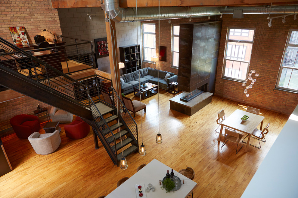 Design ideas for a mid-sized industrial loft-style family room in Minneapolis with light hardwood floors, a two-sided fireplace, a metal fireplace surround, no tv and brown floor.