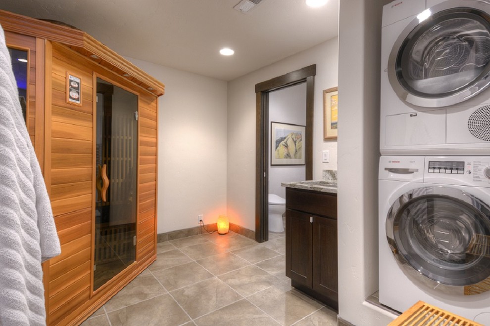 Photo of a small contemporary utility room in Other with an undermount sink, shaker cabinets, dark wood cabinets, quartzite benchtops, grey walls, porcelain floors and a stacked washer and dryer.