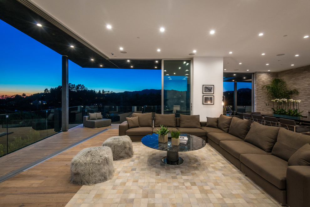 This is an example of an expansive contemporary open concept living room in Los Angeles with light hardwood floors, a ribbon fireplace, a stone fireplace surround and a wall-mounted tv.