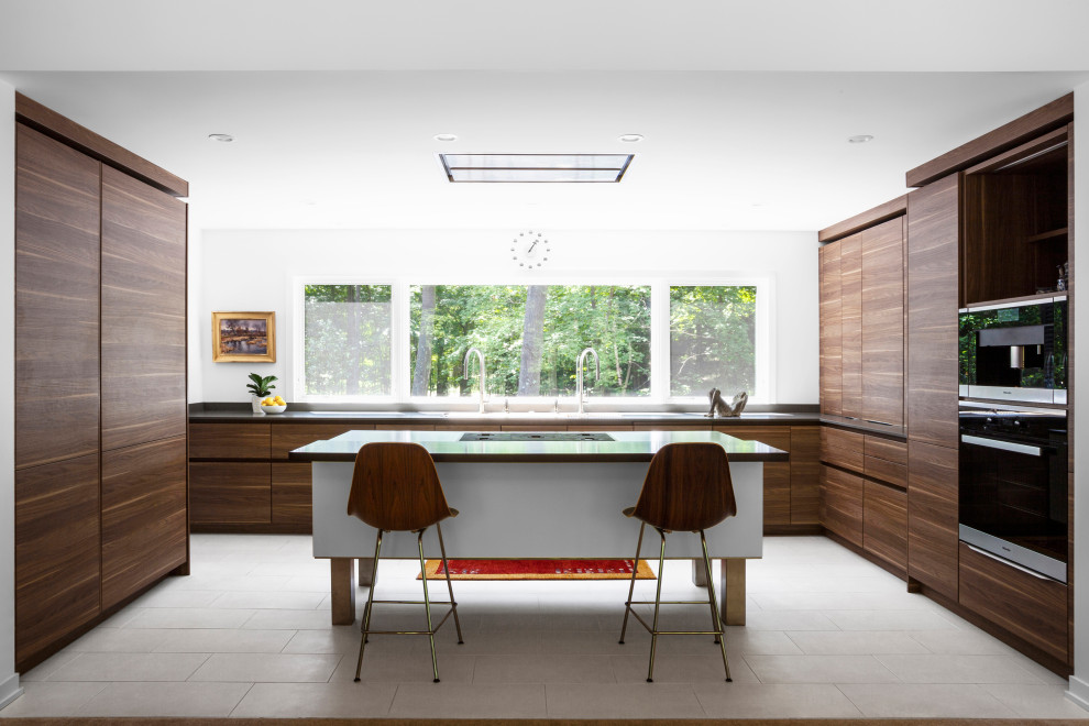 This is an example of a mid-sized midcentury u-shaped kitchen pantry in Grand Rapids with a triple-bowl sink, flat-panel cabinets, medium wood cabinets, quartz benchtops, grey splashback, engineered quartz splashback, panelled appliances, porcelain floors, with island, white floor and grey benchtop.