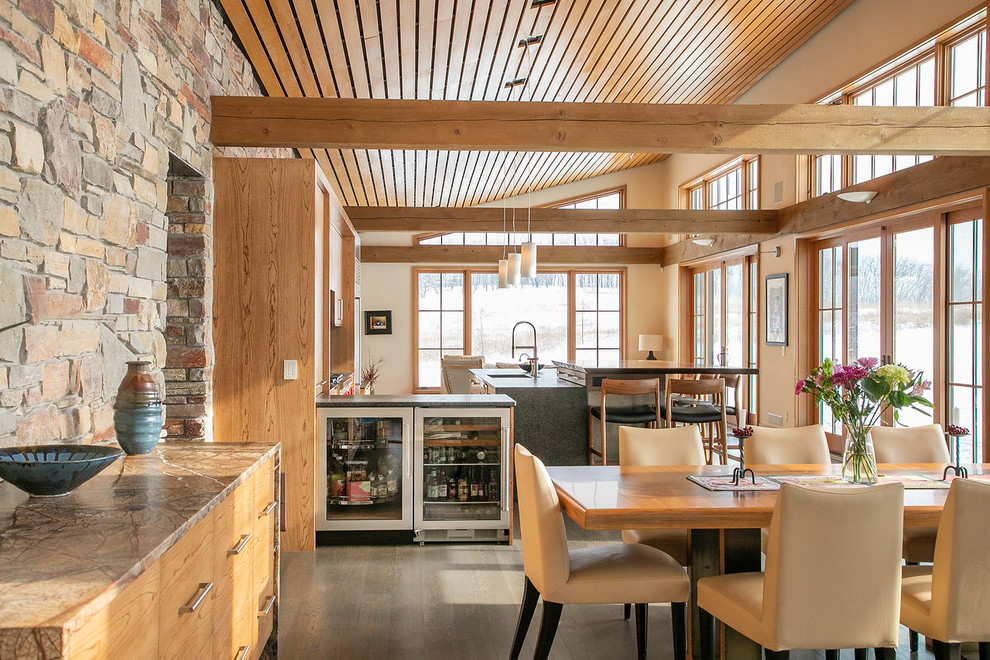 Large mountain style l-shaped medium tone wood floor and brown floor open concept kitchen photo with flat-panel cabinets, light wood cabinets, granite countertops, black backsplash, stainless steel appliances, an island, black countertops, a double-bowl sink and porcelain backsplash