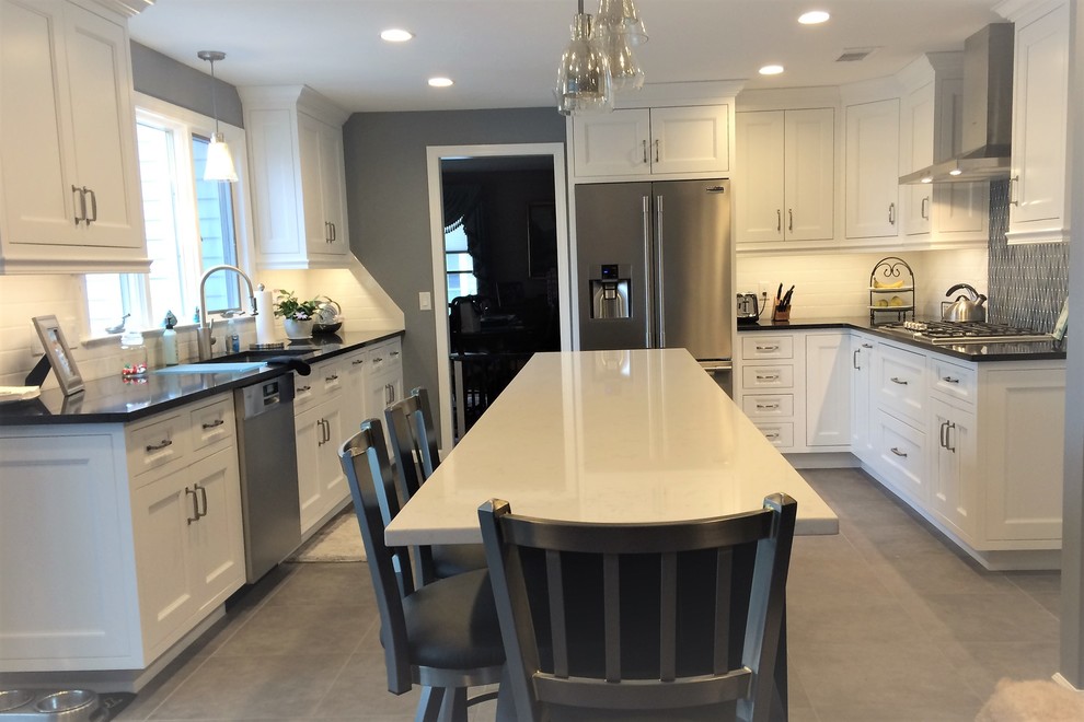 Example of a large transitional galley porcelain tile and gray floor open concept kitchen design with an undermount sink, recessed-panel cabinets, white cabinets, quartz countertops, blue backsplash, mosaic tile backsplash, stainless steel appliances, an island and black countertops