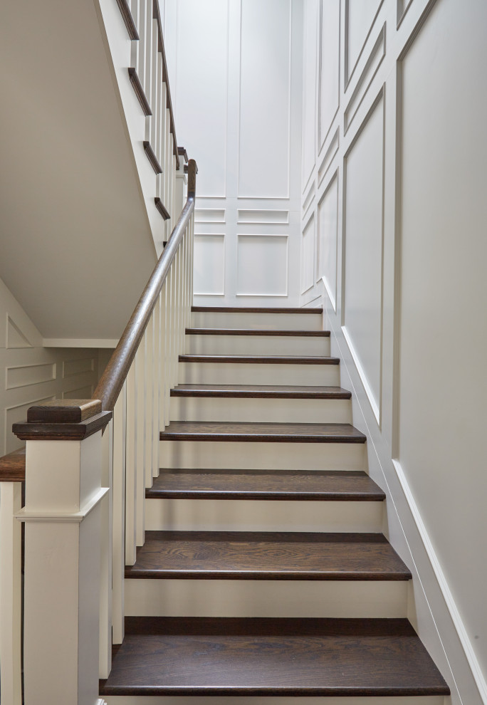 Пример оригинального дизайна: большая п-образная лестница с деревянными ступенями, крашенными деревянными подступенками, деревянными перилами и панелями на части стены