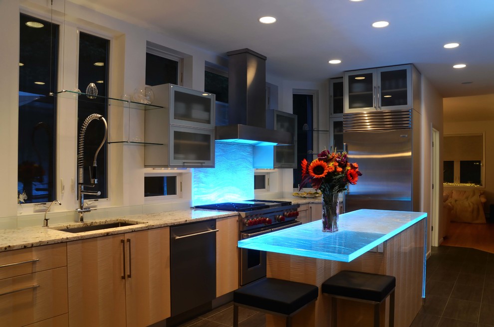 Contemporary l-shaped eat-in kitchen in New York with an undermount sink, flat-panel cabinets, light wood cabinets, glass benchtops, white splashback, glass tile splashback, stainless steel appliances and blue benchtop.