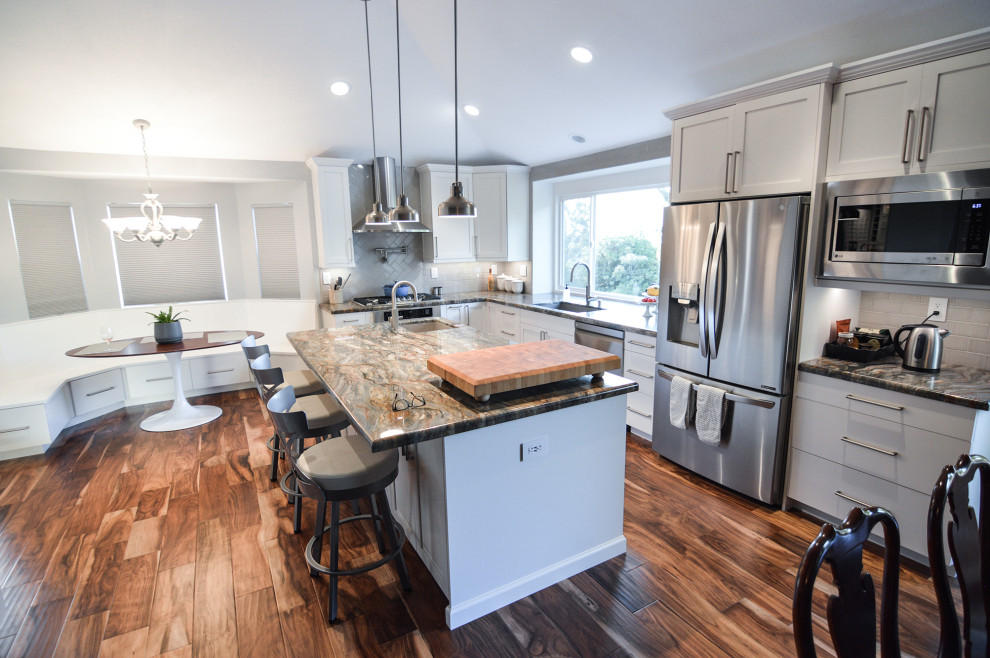 Large transitional l-shaped medium tone wood floor and brown floor eat-in kitchen photo in Los Angeles with a single-bowl sink, shaker cabinets, white cabinets, quartzite countertops, white backsplash, porcelain backsplash, stainless steel appliances, an island and multicolored countertops
