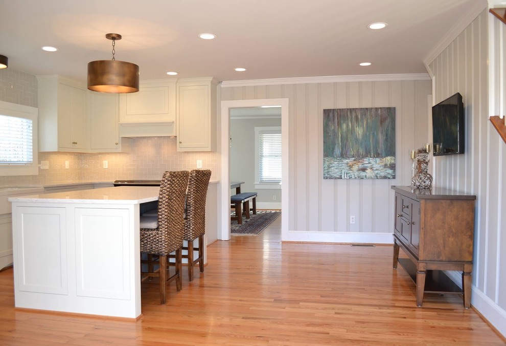 Example of a mid-sized transitional u-shaped light wood floor open concept kitchen design with a farmhouse sink, recessed-panel cabinets, white cabinets, quartz countertops, beige backsplash, ceramic backsplash, stainless steel appliances and an island