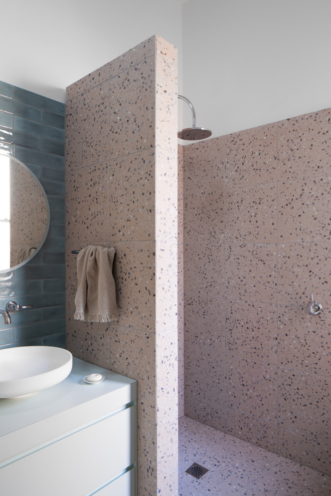 Photo of a medium sized bohemian ensuite bathroom in Melbourne with flat-panel cabinets, blue cabinets, a built-in bath, a walk-in shower, a two-piece toilet, pink tiles, stone tiles, pink walls, terrazzo flooring, a vessel sink, laminate worktops, pink floors, an open shower, blue worktops, a laundry area, a single sink and a built in vanity unit.