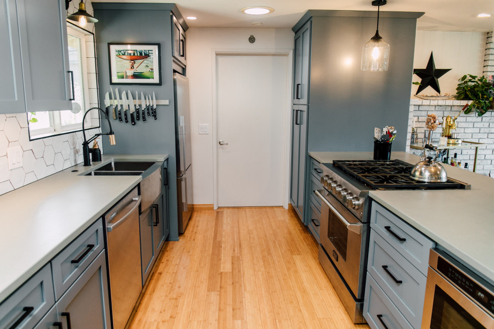 Small eclectic galley open plan kitchen in Seattle with a farmhouse sink, shaker cabinets, blue cabinets, quartz benchtops, white splashback, ceramic splashback, stainless steel appliances, bamboo floors, brown floor and grey benchtop.
