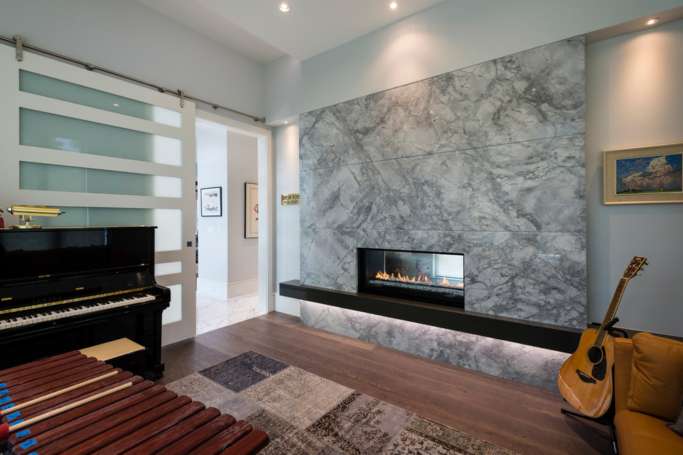 Photo of a mid-sized contemporary home studio in Vancouver with grey walls, medium hardwood floors, a two-sided fireplace, a stone fireplace surround and brown floor.