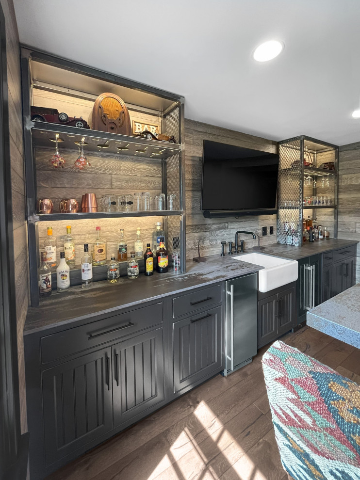 Photo of a large traditional home bar in Philadelphia with an integrated sink, beaded inset cabinets, black cabinets, quartzite benchtops, brown splashback, shiplap splashback, brown benchtop, medium hardwood floors and brown floor.