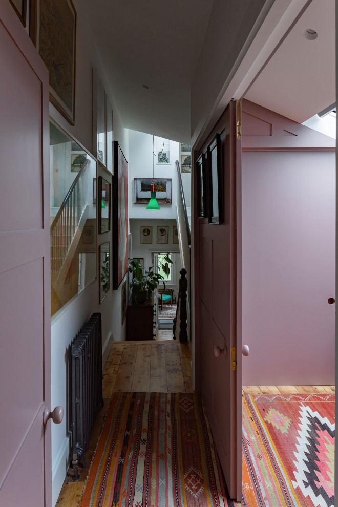 Ispirazione per un soggiorno eclettico di medie dimensioni e aperto con libreria, pareti rosa, pavimento in legno massello medio, TV nascosta e pannellatura