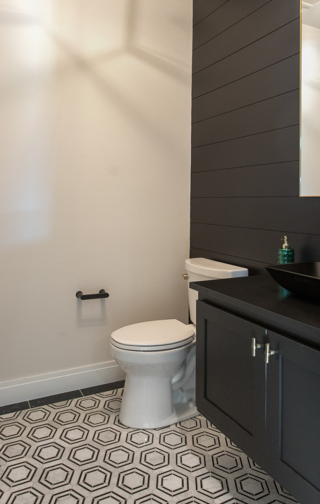 Modern inredning av ett svart svart toalett, med släta luckor, svarta skåp, en toalettstol med separat cisternkåpa, mosaikgolv, ett fristående handfat och flerfärgat golv