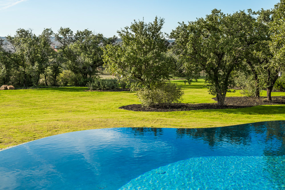 This is an example of an expansive traditional backyard custom-shaped infinity pool in Austin with natural stone pavers.