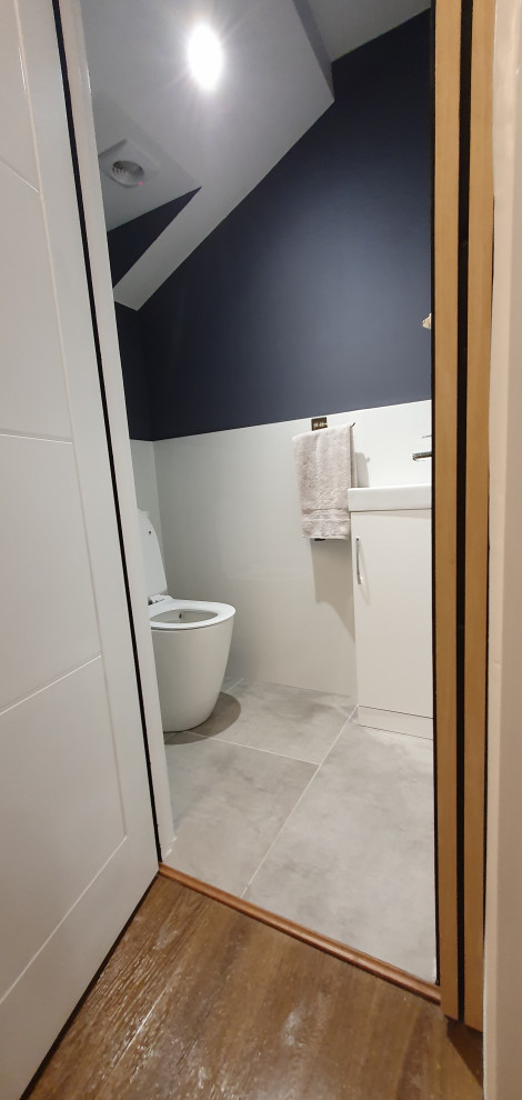 Photo of a small contemporary cloakroom in London with freestanding cabinets, white cabinets, a one-piece toilet, white tiles, porcelain tiles, porcelain flooring, grey floors, a feature wall, a freestanding vanity unit and blue walls.