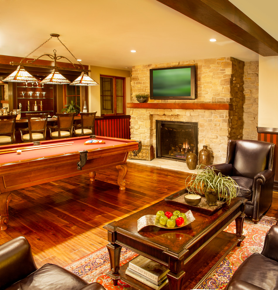 This is an example of a mediterranean fully buried basement in Los Angeles with beige walls, medium hardwood floors, a standard fireplace, a stone fireplace surround and brown floor.