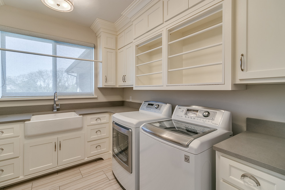This is an example of a mid-sized country l-shaped dedicated laundry room in Oklahoma City with a farmhouse sink, flat-panel cabinets, white cabinets, quartz benchtops, beige walls, porcelain floors, a side-by-side washer and dryer and grey floor.