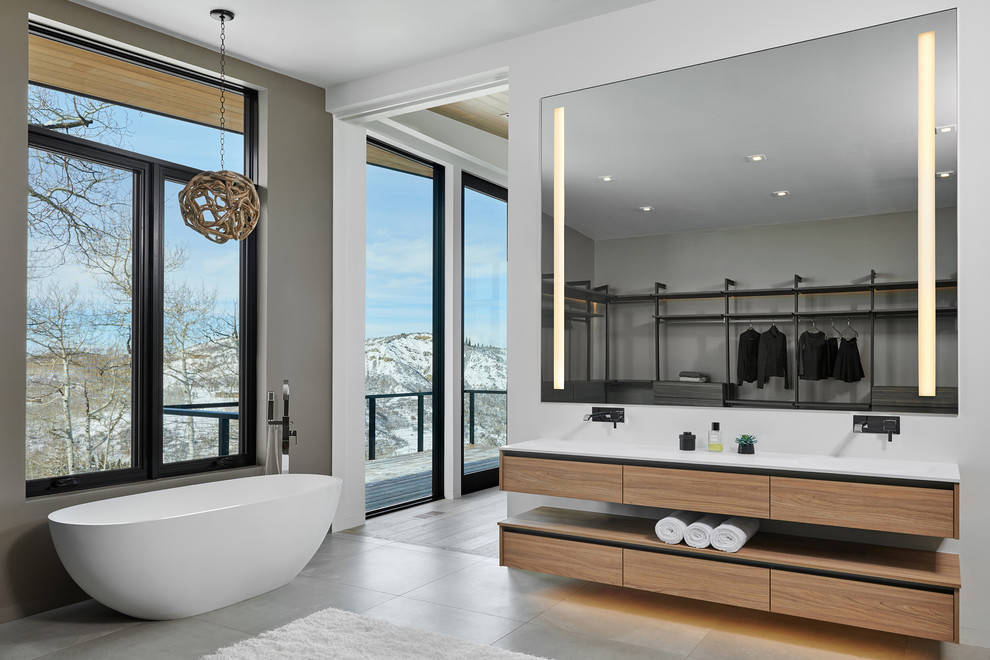 Design ideas for a large contemporary master bathroom in Denver with a freestanding tub, porcelain floors, grey floor, flat-panel cabinets, medium wood cabinets, a one-piece toilet, gray tile, cement tile, grey walls, an integrated sink, solid surface benchtops and white benchtops.