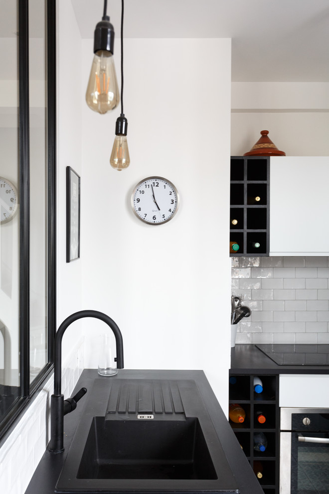 Inspiration for a small modern u-shaped open plan kitchen in Paris with a drop-in sink, flat-panel cabinets, white cabinets, solid surface benchtops, white splashback, subway tile splashback, black appliances, cement tiles, no island, grey floor and black benchtop.