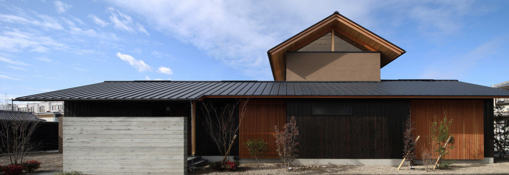 Réalisation d'une grande façade de maison marron asiatique en bois et planches et couvre-joints à un étage avec un toit à deux pans, un toit en métal et un toit noir.