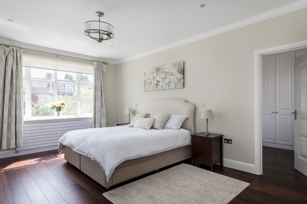 Design ideas for a mid-sized traditional master bedroom in London with beige walls, dark hardwood floors, no fireplace and brown floor.